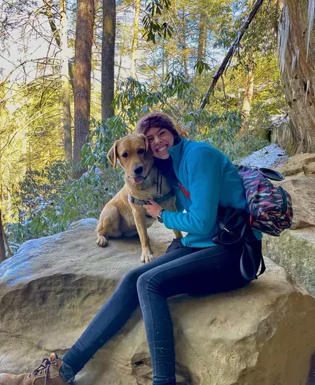 A woman holding a dog sitting on a rock in the woods