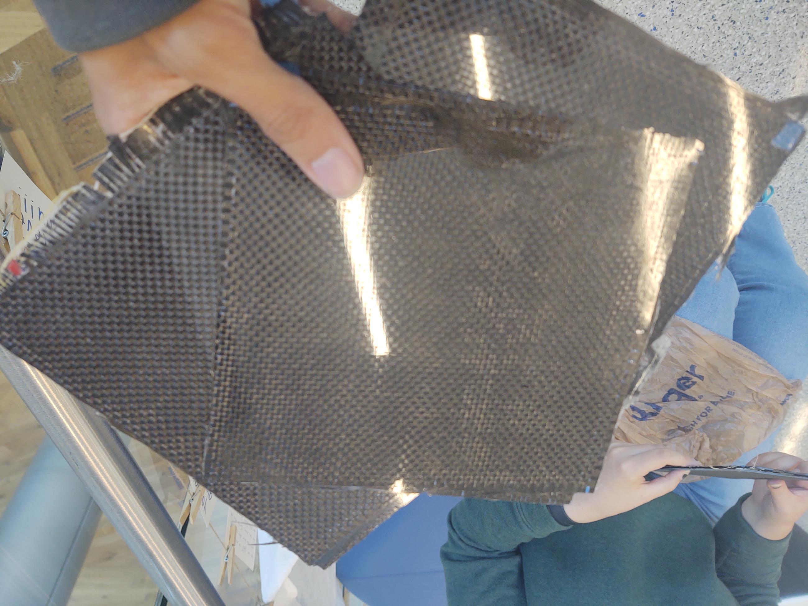 Image of hand holding 3 square sheets of carbon fiber